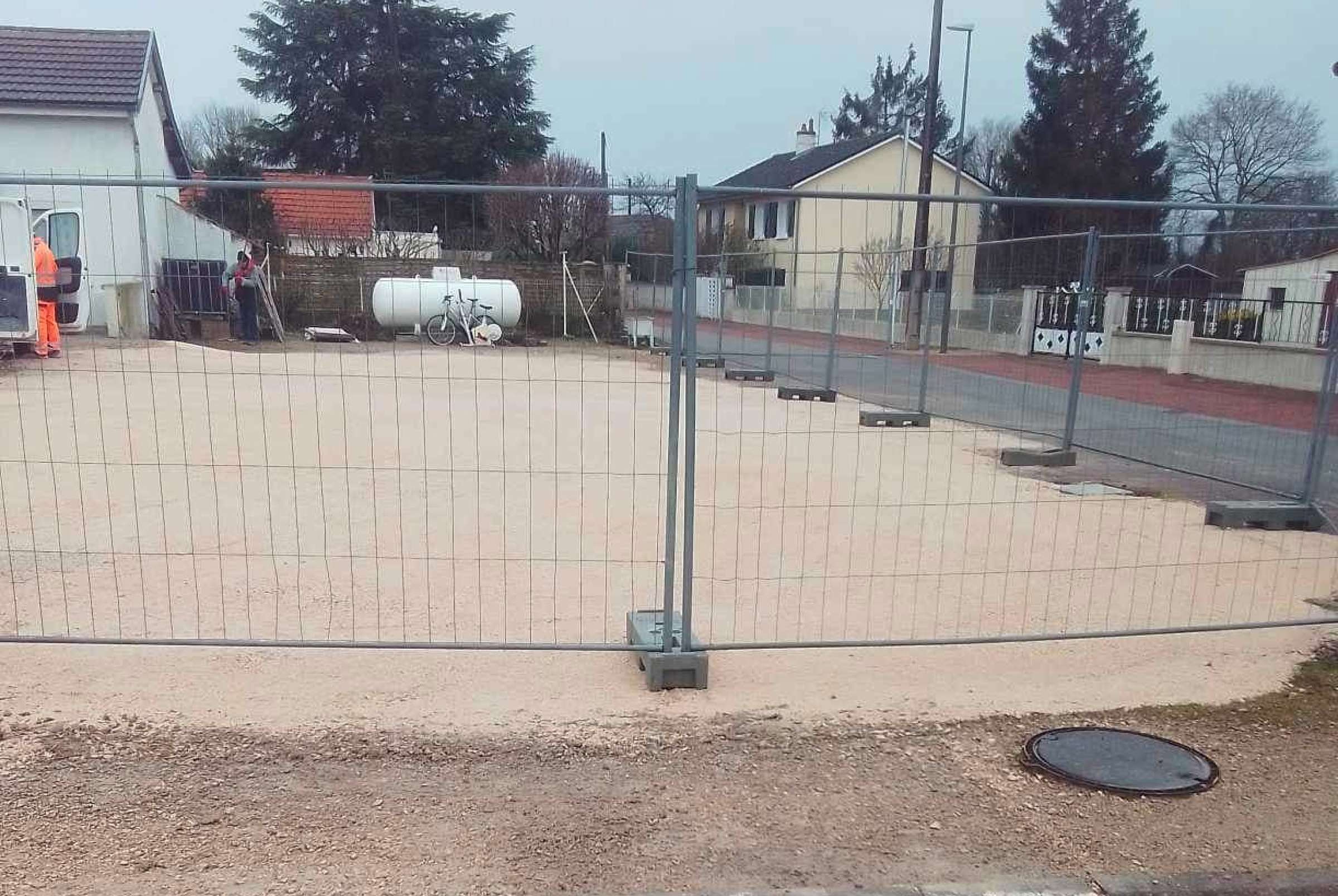 Terrain de lotissement viabilisé et sécurisé par des barrières de chantier, avec cuve de gaz et camion d’intervention en arrière-plan.