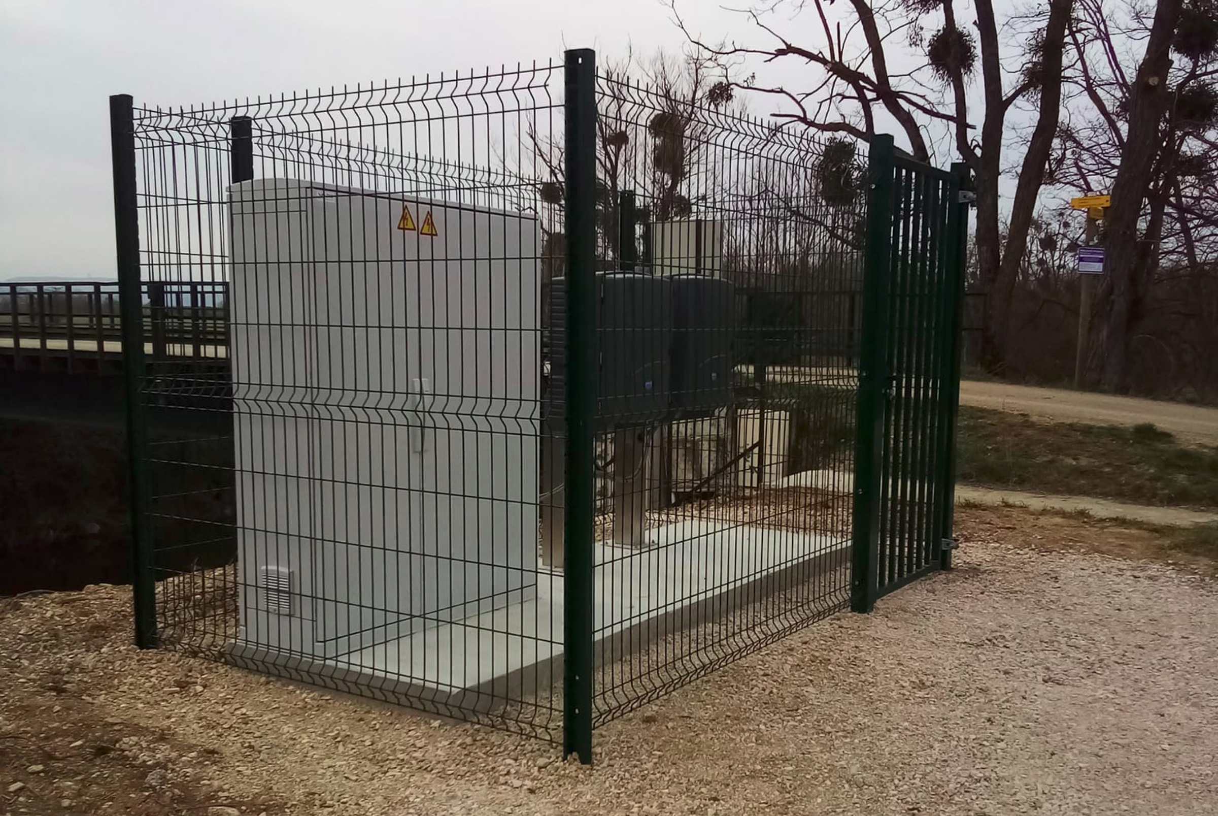 Clôture rigide verte avec portillon sécurisant un poste électrique technique en bordure de voie.