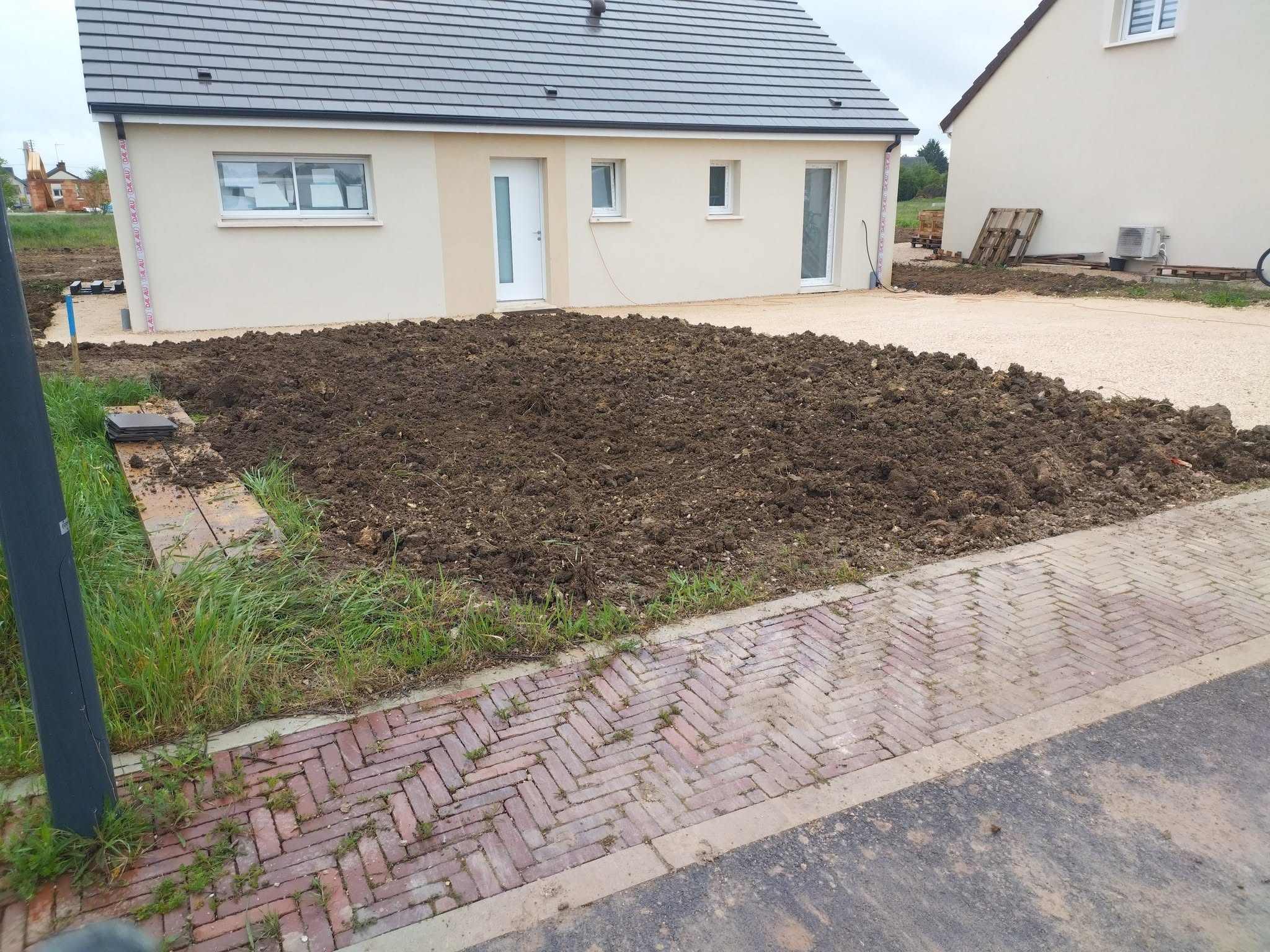 Terrain remis en forme devant une maison neuve, allée gravillonnée et bordure pavée.
